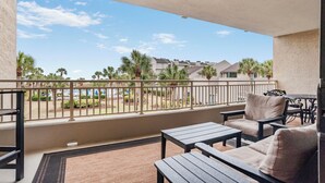 A balcony with a view of a pool and palm trees, furnished with a table and chairs. - Shorewood 234-Freshly Updated in 2025 3BR Oceanview Near Shops & Restaurants (Hilton Head Island)