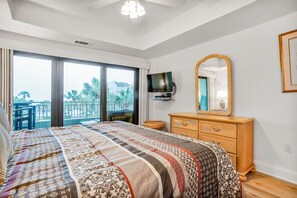 Una camera da letto con un letto grande, una cassettiera in legno, una televisione e un balcone con vista sulle palme.