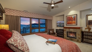 A hotel room with a large bed, a fireplace, a television, and a scenic view through the windows.