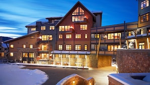 A multi-story hotel with a ski resort exterior, featuring balconies, large windows, and a stone facade.