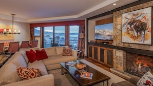 A modern living room with a large sofa, a fireplace, a television, and a view of a snowy landscape through large windows.
