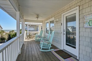 Eine überdachte Veranda mit Schaukelstühlen, eine Tür mit Fenster und Blick auf den Ozean.