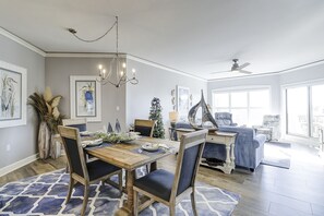 Uma sala de jantar com uma mesa de madeira, cadeiras e um candelabro. Há um pinheiro de Natal e uma decoração de barco à vela.