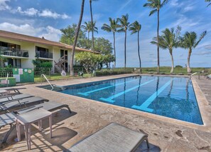 A swimming pool with lounge chairs, palm trees, and a building with a balcony.