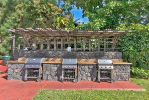 A barbecue setup with a stone wall and a wooden pergola.