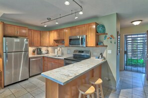 A modern kitchen with wooden cabinets, stainless steel appliances, a granite countertop, and a bar stool.