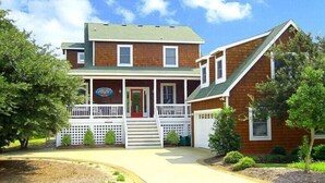A two-story house with a front porch, a garage, and a well-maintained lawn. - Waves of Grace: Private Pool, Hot Tub, Screened Porch (Corolla)