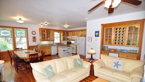 A spacious living room with a beige leather sofa, a wooden coffee table, and a dining area with a wooden table and chairs. - Waves of Grace: Private Pool, Hot Tub, Screened Porch (Corolla)
