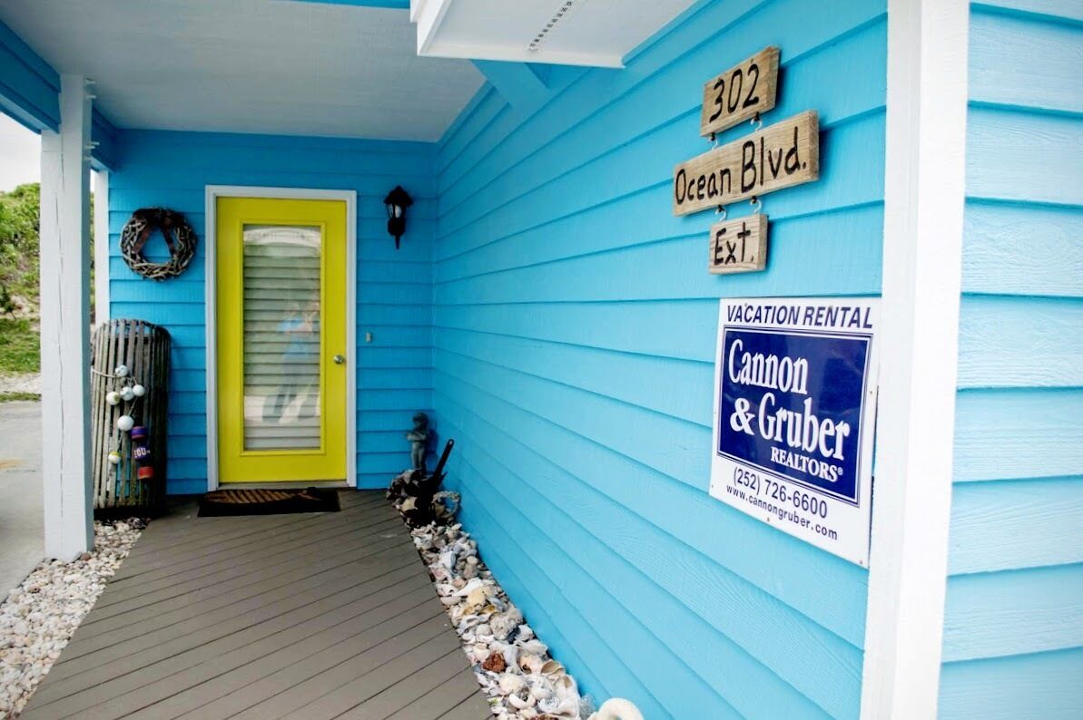 Il s’agit d’une maison de vacances à louer, reconnaissable à sa façade d’un bleu éclatant, à sa porte jaune et à une enseigne indiquant « 302, Ocean Blvd. Ext. », ainsi qu’à une autre enseigne indiquant « Location de vacances » pour l’agence immobilière « Cannon & Gruber ».
