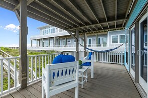 Eine Holzterrasse mit weißen Geländern, einer Hängematte und zwei weißen Stühlen mit blauen Kissen.