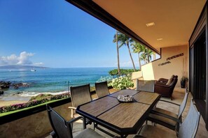 A balcony with a table and chairs overlooking a beach and ocean.