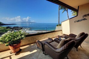 A balcony with wicker furniture, a potted plant, and a view of the ocean. - Gorgeous Oceanfront Sanctuary – Makena Surf #G-204 - Breathtaking Views! (Makena, Maui)