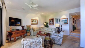 A living room with a ceiling fan, a sofa, a coffee table, and a TV mounted on the wall.