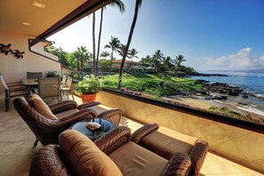 A balcony with wicker furniture, a view of the ocean, and a tropical landscape.