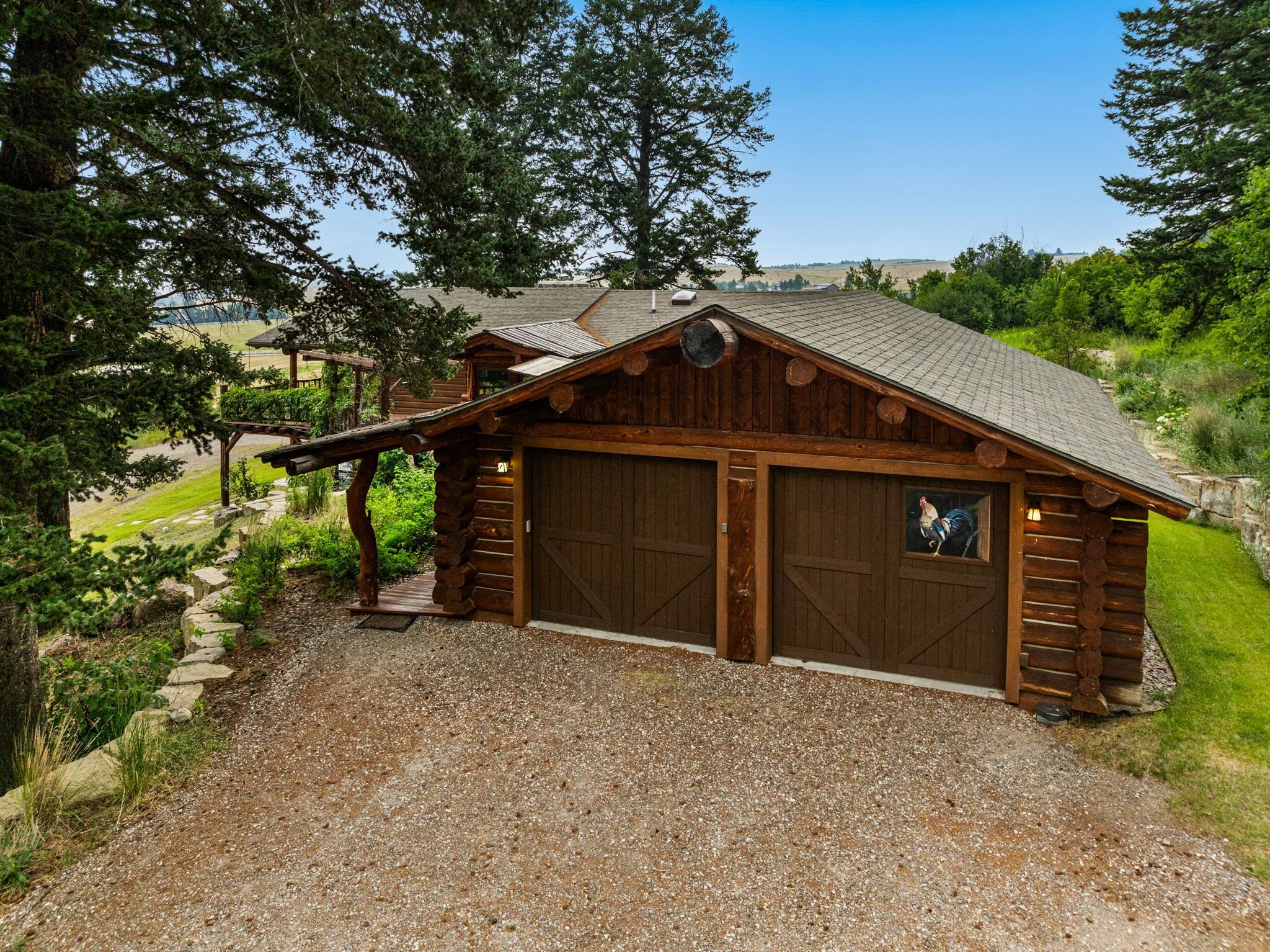A rustic wooden cabin with a gravel driveway, large garage doors, and a covered porch.