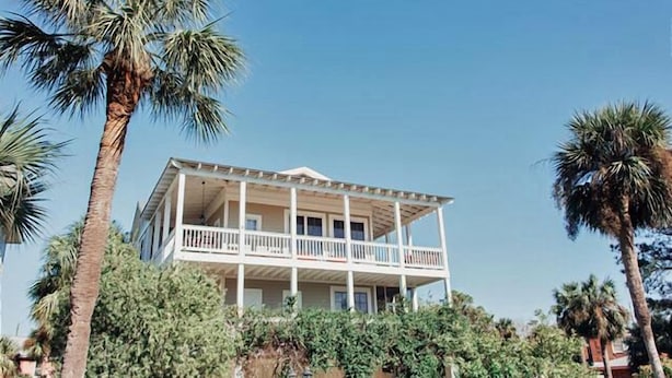 Una casa de dos pisos con balcón, rodeada de palmeras.