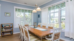 Un comedor con una mesa de madera, sillas blancas y una estantería.
