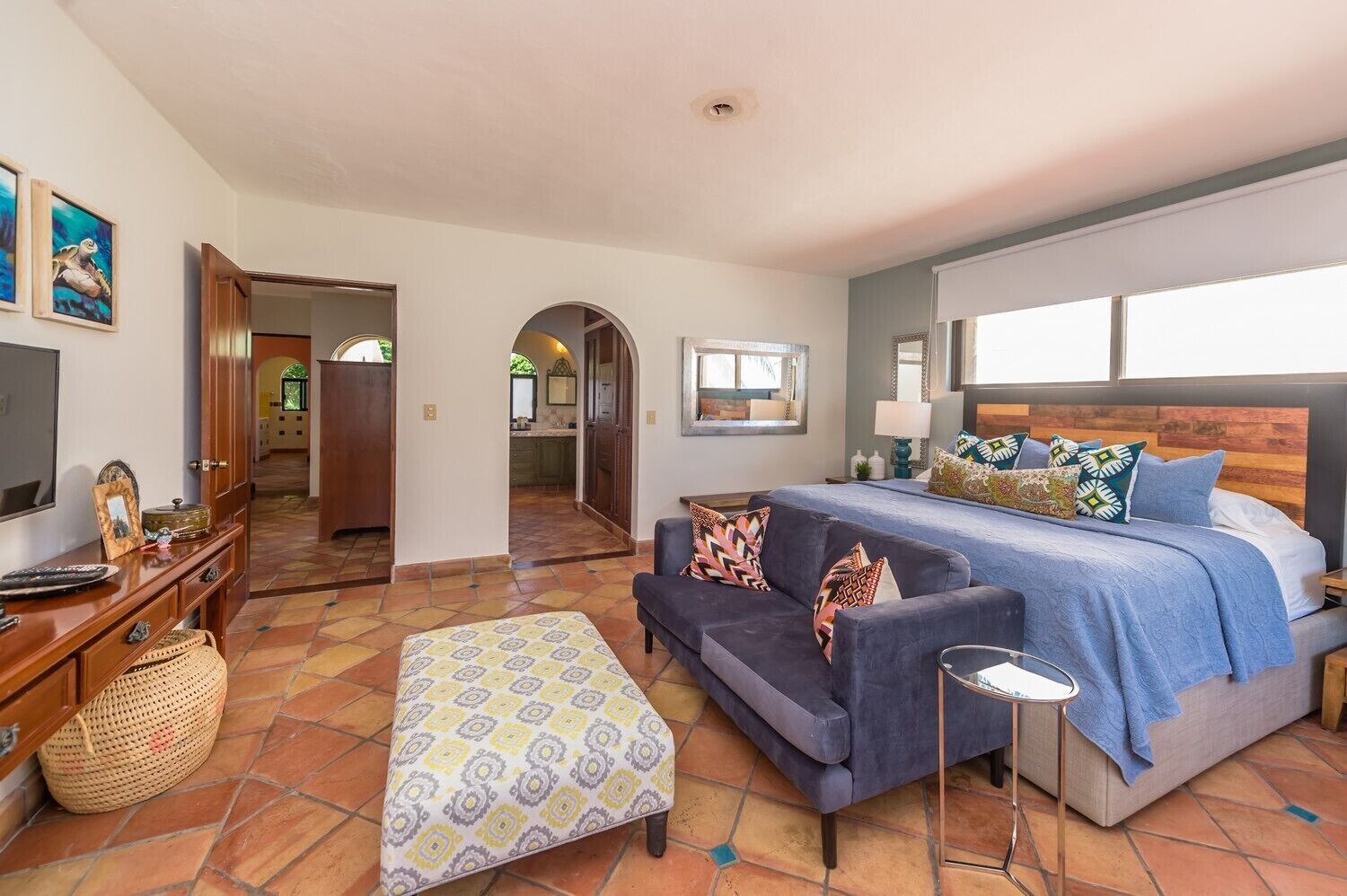 A hotel room with a bed, sofa, and TV. There is a hallway leading to a kitchen and a bathroom.