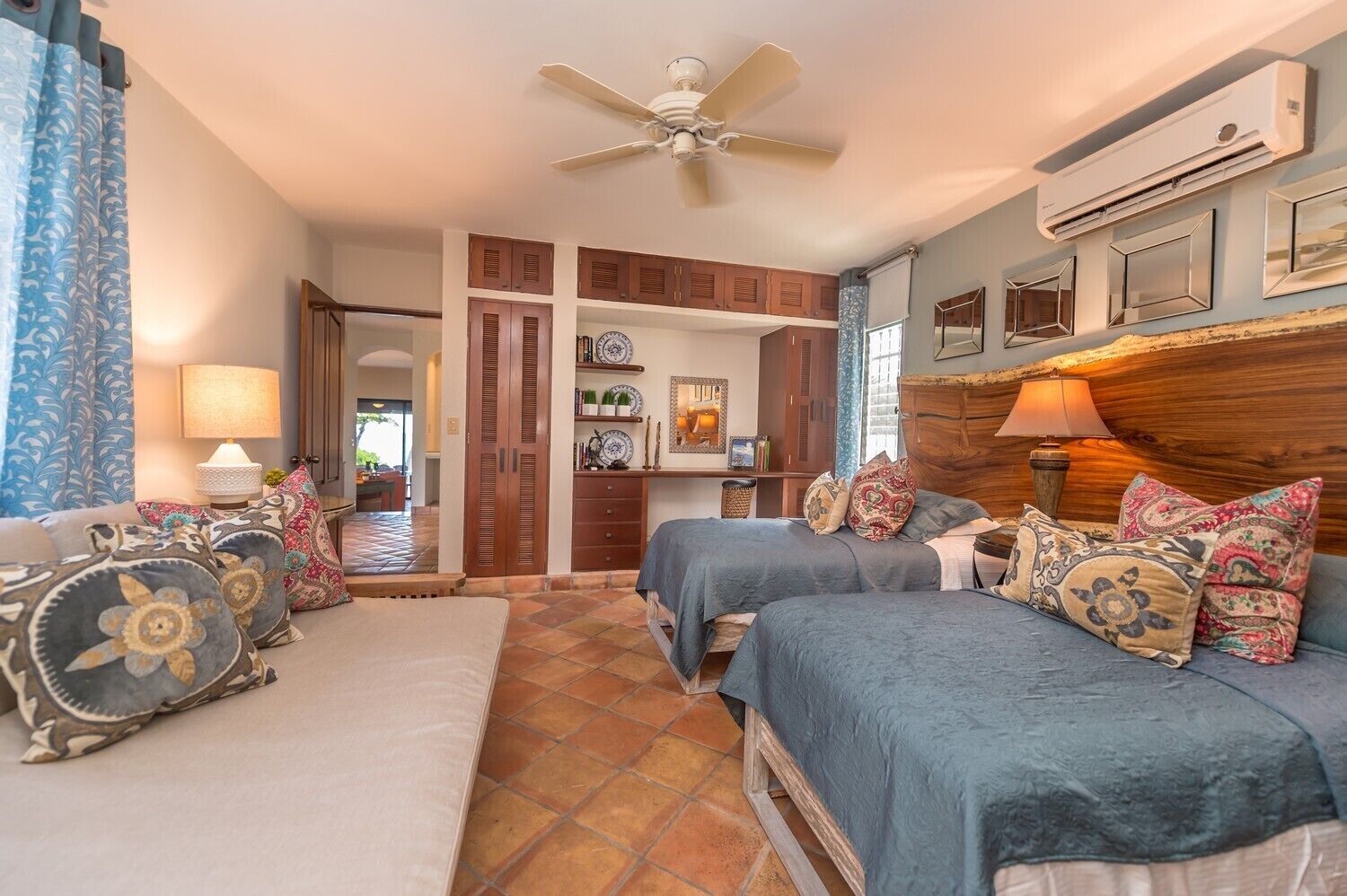 A bedroom with two beds, a ceiling fan, an air conditioning unit, and a view of the kitchen.