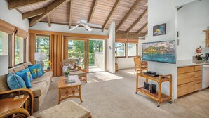 A spacious living area with a sofa, chairs, a coffee table, and a TV. There is a sliding glass door leading to an outdoor area.