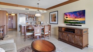 A modern living room with a wooden dining table, chairs, a TV, and a large painting. - Maui Resort Rentals: Hyatt Residence Club – 2BR Oceanfront Middle Floor VIlla (Lahaina)