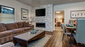 A modern living room with a stone fireplace, a flat-screen TV, and a dining area with a table and chairs.