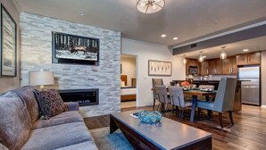 A modern living room with a fireplace, a dining area with chairs, and a kitchen with cabinets and appliances.