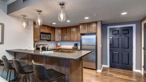 A modern kitchen with a central island, bar stools, stainless steel appliances, and pendant lighting.