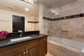 A bathroom with a dark wooden vanity, a white sink, a glass shower enclosure, and a bathtub.