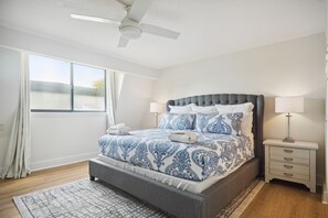 Ein Schlafzimmer mit Bett, Nachttisch, Lampe, Deckenventilator und Fenster.