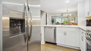 A modern kitchen with a stainless steel refrigerator, white cabinetry, and a built-in dishwasher. - Surf Court 60 - 3 Story South Forest Beach Townhouse (Hilton Head Island)
