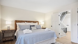 A neatly arranged bedroom with a bed, bedside tables, and a staircase leading to another room. - Surf Court 60 - 3 Story South Forest Beach Townhouse (Hilton Head Island)