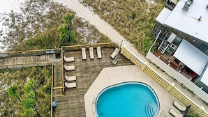 An aerial view of a pool area with a wooden deck, lounge chairs, and a swimming pool.