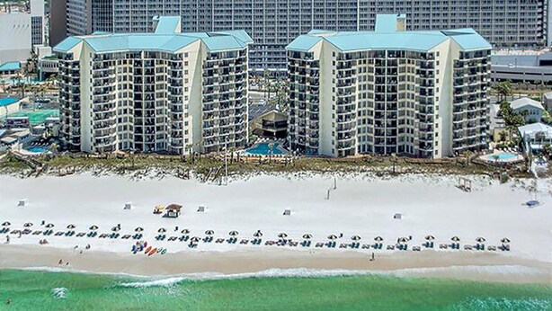 A beachfront hotel with multiple high-rise buildings, a sandy beach, and several umbrellas.