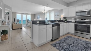 A modern kitchen with white cabinetry, a built-in dishwasher, a stainless steel oven, and a large island with a sink.