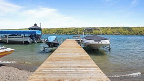 Un muelle de madera que da a un lago, con barcos amarrados a la derecha y una estructura cubierta a la izquierda.