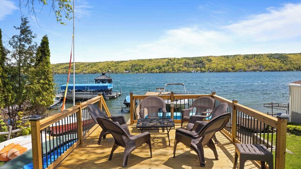 Una terraza de madera con mobiliario exterior, vista al lago y barcos al fondo.