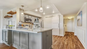 Una cocina moderna con una isla central, electrodomésticos de acero inoxidable e iluminación colgante.