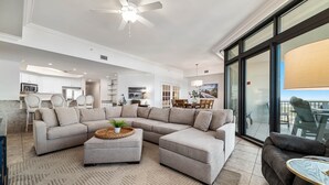 A spacious living area with a large L-shaped sectional sofa, a round coffee table, and a ceiling fan. - The Oasis at Orange Beach 2114 | Lazy River, Water Slide | My Beach Getaways (Orange Beach)