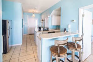 A kitchen with a central island, two barstools, a refrigerator, and a coffee maker.