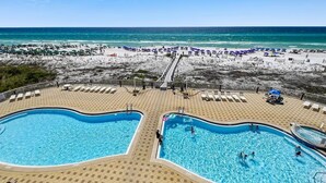 A beachside pool area with two swimming pools, lounge chairs, and umbrellas.