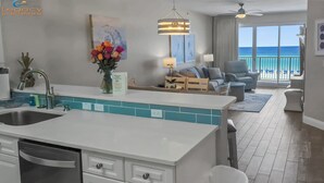 A modern kitchen with a central island, a dining area with a view of the ocean, and a living room with a sofa and armchairs.