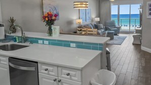 A modern kitchen with a central island, a dining area with a view of the ocean, and a living room with a sofa and armchairs. - Summer Place 405 - Beautifully Renovated 3Br Beachfront Condo (Fort Walton Beach)