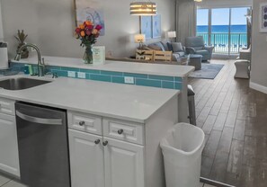 A modern kitchen with a central island, a dining area with a view of the ocean, and a living room with a sofa and armchairs. - Summer Place 405 - Beautifully Renovated 3Br Beachfront Condo (Fort Walton Beach)