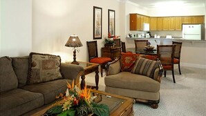 Uma sala de estar com sofá, poltrona, mesa de centro e um espaço de jantar com cadeiras e mesa.