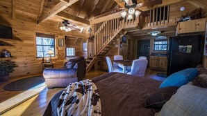 A cozy cabin interior with a wooden interior, a dining area, and a staircase leading to an upper level.