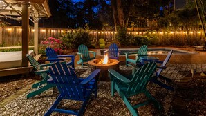 An outdoor seating area with Adirondack chairs and a fire pit. - Guiding Light Cottage | Heated Saltwater Pool (Tybee Island)