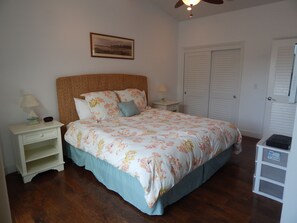 Ein Schlafzimmer mit Bett, Nachttischen, Deckenventilator und einer Tür mit Klappläden.