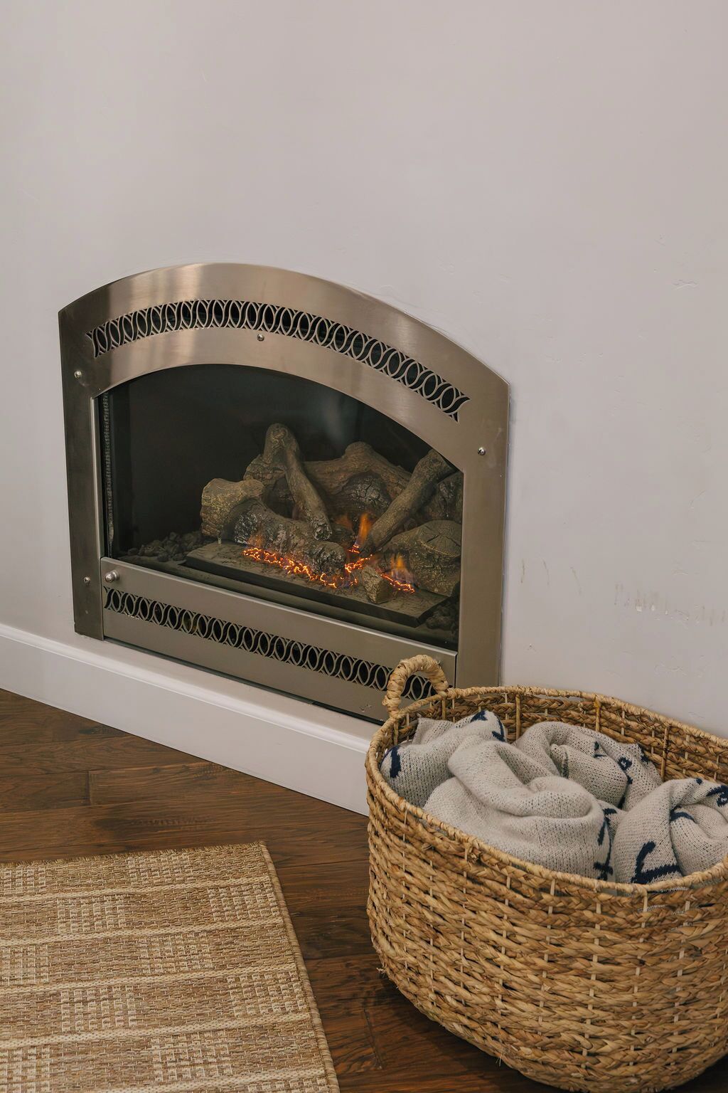 Uma lareira com moldura metálica decorativa e um cesto de mantas ao lado.