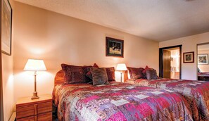 A bedroom with a large bed, two bedside tables with lamps, a framed picture on the wall, and a door leading to another room.